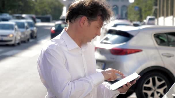 トラフィック スローモーションのクローズ アップと都市の通りでタブレットを使用して白いシャツを持つハンサムな男 — ストック動画