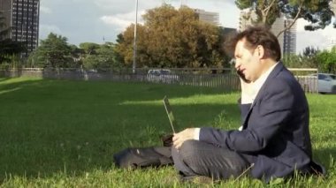 City park çimenlerin üzerinde oturan dizüstü bilgisayar ile çalışan adam