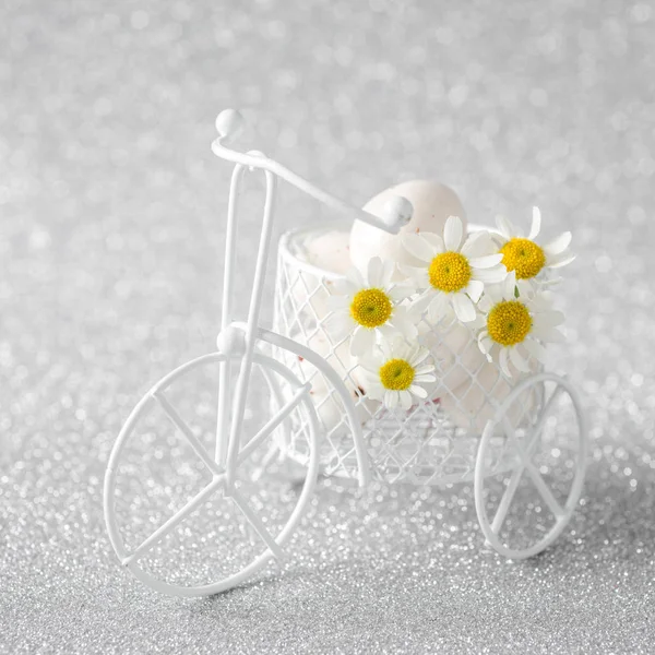 Білі шоколадні яйця та ромашки на іграшковому велосипеді на блискучому фоні. Великодній фон . — стокове фото