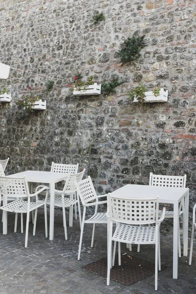 Cafe stoly a židle mimo vedle kamenné zdi. Itálie. — Stock fotografie