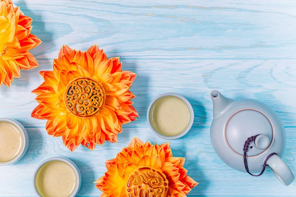 Mooncakes in a fresh orange dahlia flowers, a blue teapot and cups of green tea on a blue wooden background. Chinese mid-autumn festival food. — Stock Photo, Image