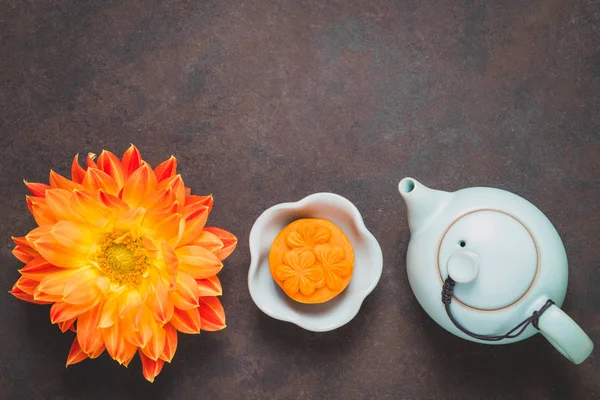 Mooncake, fresh orange dahlia flowers, a blue teapot and cups of green tea on a brown background. Chinese mid-autumn festival food. — Stock Photo, Image