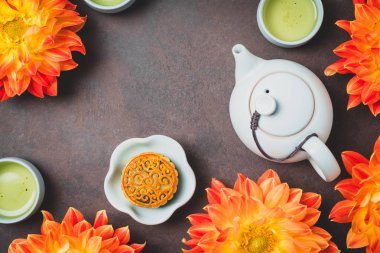 Mooncake, taze turuncu dahlia çiçekleri, mavi bir çaydanlık ve kahverengi bir arka plan üzerinde yeşil çay bardak. Çin sonbahar ortası festival gıda.