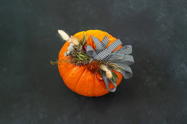 Halloween or Thanksgiving background. Autumn composition in pumpkin with ribbons and dried flowers on dark background with copy space.