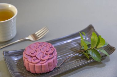Geleneksel olmayan bir Çin ay pastası. Mor Japon yer elmasından yapılmış. Siyah seramik tabakta bir fincan yeşille birlikte. Üst görünüm, gri tezgah üstü arkaplan.