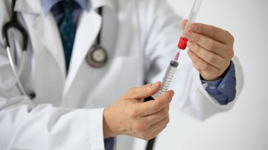 Beyaz önlüklü bir doktor şırıngalı bir kan tüpünden örnek alıyor..