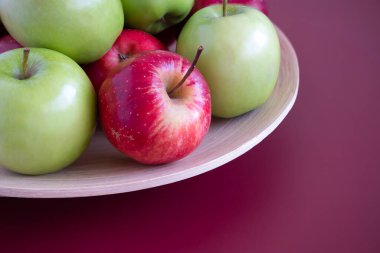Bambu tabaktaki kırmızı ve yeşil elmalara yakın çekim. Maun arkaplanı.
