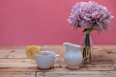 Beyaz porselen bardakta sütlü limon çayı ve süt sürahisi. Ahşap masa arkaplanı.