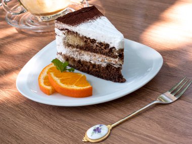 Kahverengi bir masanın üzerinde bir dilim çikolatalı kek ve arka planda boş bir fincan kahve..