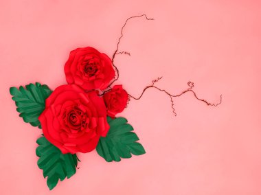 Kırmızı kağıt güller ve somon pembe arka planda ince dallar.