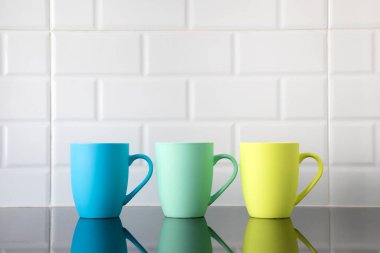 Siyah granit mutfak masasında renkli kahve fincanları ve tezgahın temiz yüzeyinde yansımaları var..