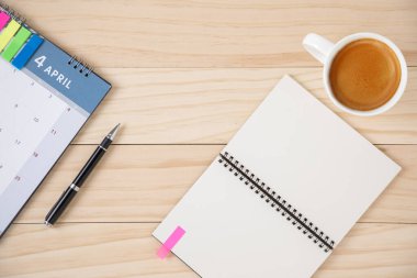 Boş bir defter, bir takvim ve beyaz seramik bardakta bir fincan kahve. Ahşap arkaplan.