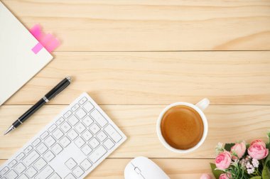 Beyaz kablosuz bilgisayar faresi ve beyaz seramik bardakta kahve bulunan klavyesi olan minimal bir çalışma alanı. Ofis tablosu kopya alanı ile yukarıdan görüntüleniyor.