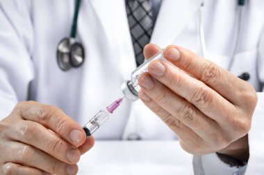 Erkek bir doktor, şişeden sıvı ya da aşı almak için şırınga kullanıyor. İlaç ya da aşı yönetimi konsepti. Covid aşı konsepti. Asya etnik kökeni.