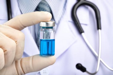 Beyaz önlüklü bir doktor mavi sıvı içeren bir ilaç şişesi tutuyor. Aşı, kavram kavgası Tarım virüsü coivid-19.