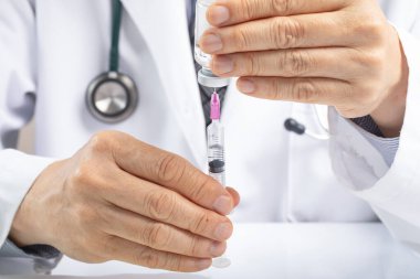 Erkek bir doktor, şişeden sıvı ya da aşı almak için şırınga kullanıyor. İlaç ya da aşı yönetimi konsepti. Covid aşı konsepti. Asya etnik kökeni.