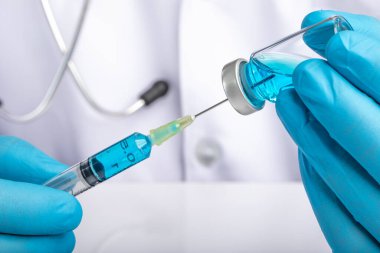 Beyaz önlüklü bir doktor, açık mavi bir sıvıyı bir şırıngadan şırıngaya çekiyor. İlaç veya aşı yönetimi, covid-19 önleme kavramı. 
