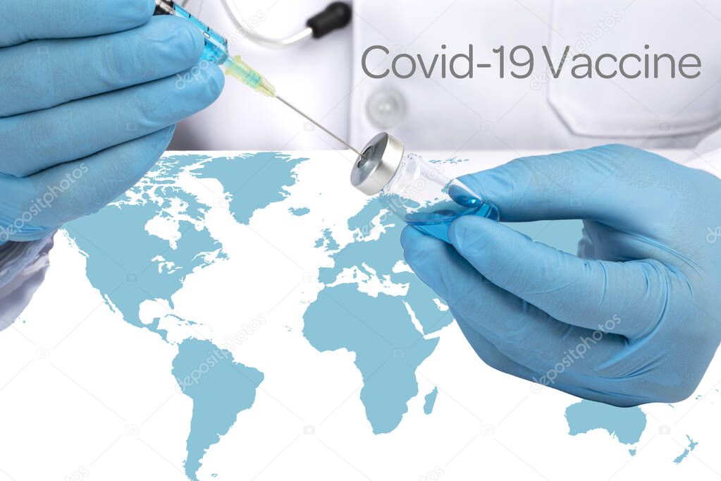A doctor in white coat sitting at a desk with blue world map drawing blue liquid from a glass vial.  World wide Covid 19 vaccination concept.