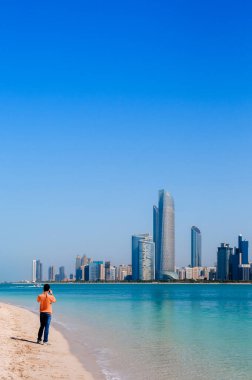 2 Şubat 2015 Abu Dabi, BAE - Beyaz kumsal mavi denizde Avrupalı turistler Abu Dabi ufuk çizgisi ve marina adasından şehir manzarası