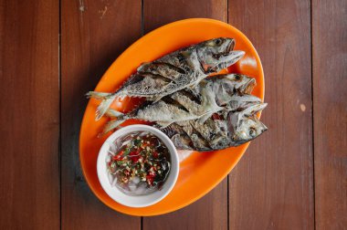 Yemek masasında Tayland yemeği, ahşap masadaki renkli tabakta kızarmış uskumru balığı.