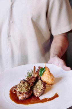 Garson kızarmış kuzu pirzolası, et suyu ve kızarmış patates servis ediyor. Yakın çekim.