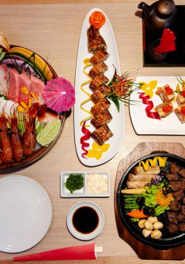 Japon Unagi Maki dürümü, Sashimi, Teppanyaki bifteği, somon balığı üst çekimde ahşap masaya.