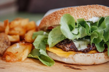 Biftekli çizburger, patates kızartması ve ahşap tabakta sos. Yakın çekim.