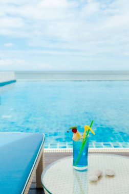 Kumsalda havuz kenarında mavi italyan gazozu, yazları tropikal tatil beldesi rahatlama konsepti.