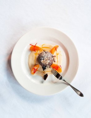 Fransız tatlısı. Vanilya soslu çikolatalı lav keki, turunçgil ve beyaz tabakta altın yaprak ve çatal üst manzara.