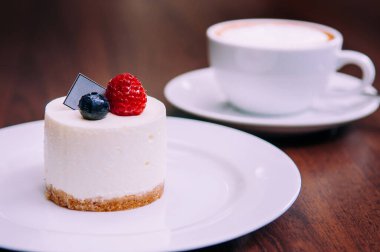 Kremalı cheesecake, yanında ahududu ve yaban mersinli, beyaz tabakta, Bekery Cafe 'de. Yemek çekimini kapat.