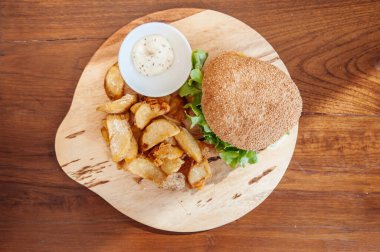 Biftekli çizburger, ahşap tabakta soslu kızarmış patates parçaları.