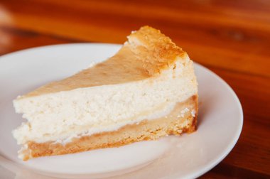 Taze fırınlanmış peynirli turta, beyaz tabakta, ahşap masada. Tüm şeftaliyi kapatın. Güzel bir dilim peynirli pasta.