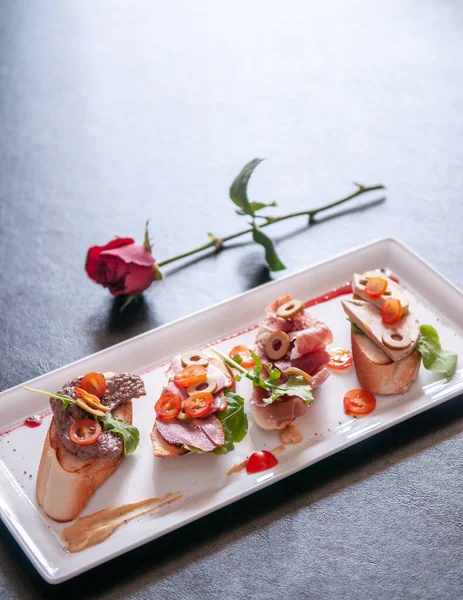 İtalyan iştah açıcı Carpaccio ekmeği kaz ciğeri ve zeytin, domates, pamaham, füme ördek, biftek ve kızılcık sosu beyaz tabakta.