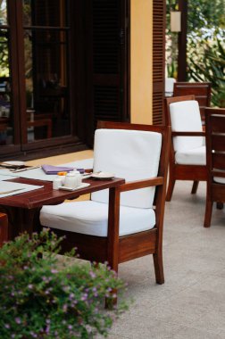 Açık havada tahta sandalyeler, yemek masası ve çiçek çalısı. Tropikal ev açık hava yaşam alanı