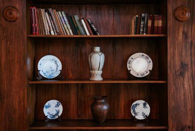 Eski kitaplarla ahşap kitaplık ve mavi desenli eski Chinaware tabaklar, seramik vazo ve bakır kavanoz.