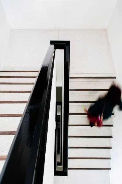 妇女走在现代风格的白色混凝土楼梯上 头顶上挂着黑色木制扶手 — 图库照片