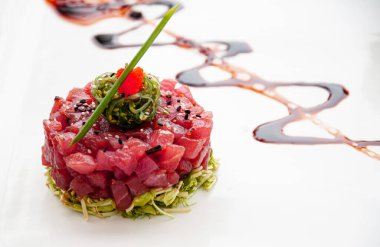 Taze ton balığı susamlı deniz yosunu ve yeşil salata ve balzamik azaltma sosu ve beyaz tabakta tropikal meyve sosu.