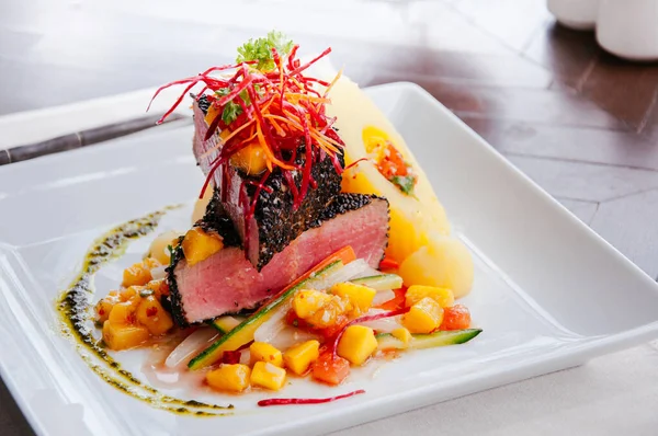 Kurutulmuş Ahi Tuna Cajun usulü susam kabuğu, tatlı ve ekşi mango salatası ve beyaz tabakta fırında patates.