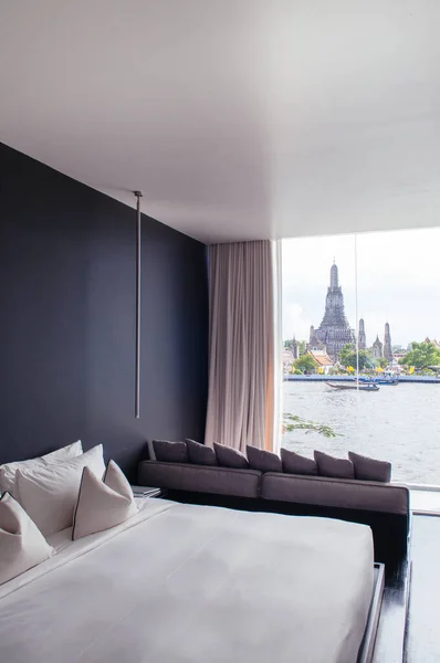 MAY 08, 2013 Bangkok, THAILAND - Bedroom with black wall white bed, pillows couch, lamp. Bay window with Wat Arun Temple view. Bangkok boutique hotel modern urban interior.