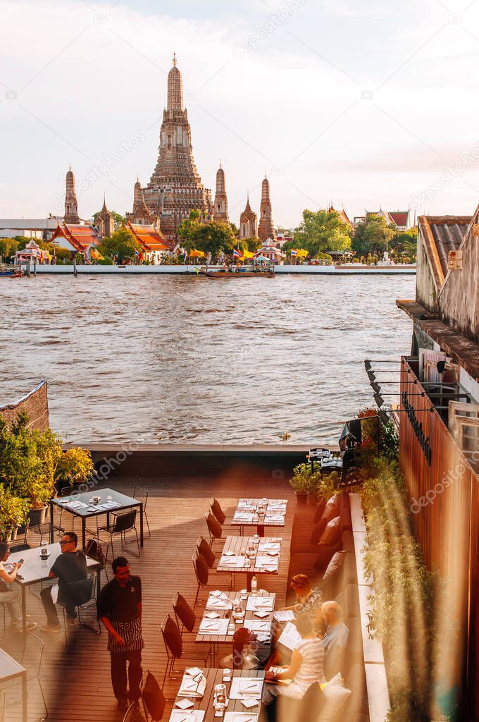 MAY 8,2013 Bangkok, THAILAND - Tourists dining at outdoor restaurant with dinner tables by river with Wat Arun temple view, natural sunlight and reflecttion on window glass