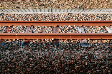 Eski paslı tren yolu ahşap kirişli ve güneş ışığı altında taşlı gölgeli.