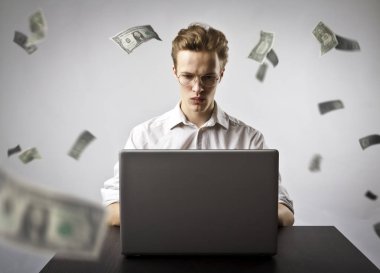 Net göz atmak için bir dizüstü bilgisayar kullanan genç adam. Genç bir işçi ve düşen Doları banknot. Para birimi ve iş kavramı.