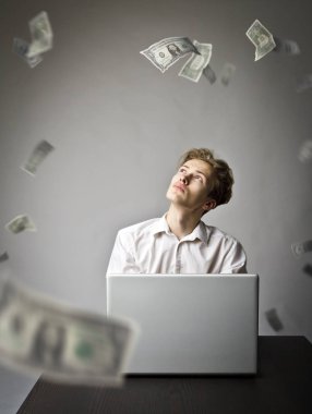Net göz atmak için bir dizüstü bilgisayar kullanan genç adam. Genç bir işçi ve düşen Doları banknot. Para birimi ve iş kavramı.