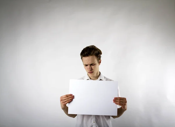 Een jongeman met wit papier in zijn handen. Ongelukkig man.. — Stockfoto