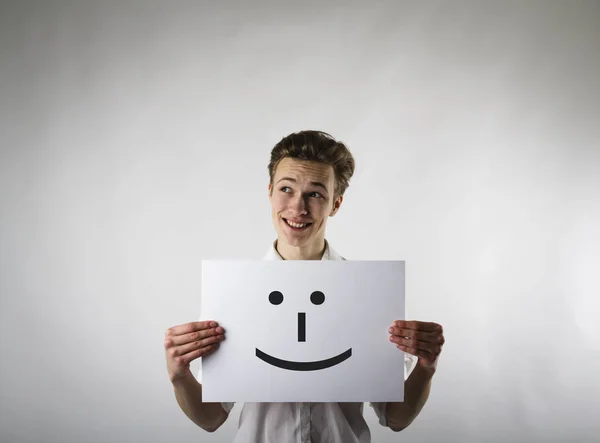 Der junge Mann hält lächelnd weißes Papier in der Hand. glücklicher Mann. — Stockfoto