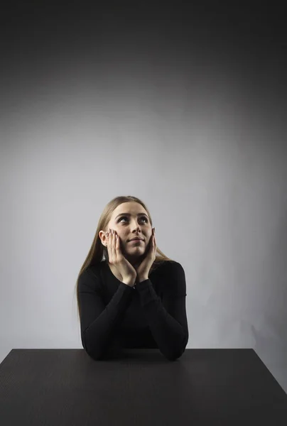 Mujer joven de negro está sentada a la mesa . —  Fotos de Stock