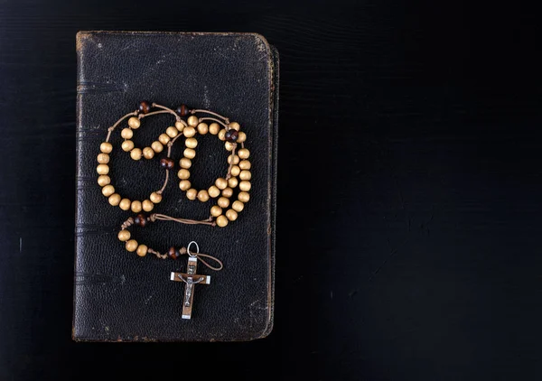 Rosary beads and prayer book on dark background.