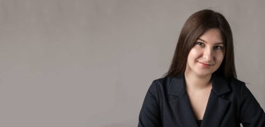 Gri arka planda gülümseyen ve kameraya bakan güzel esmer kadının portresi. Stüdyo çekimi.