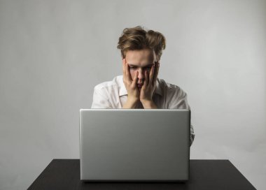 Beyazlar içindeki bilgisayarlı sinirli ve yorgun genç adam. Beyazlı adam internette dolaşmak için dizüstü bilgisayar kullanıyor. Evde öğreniyorum. İfadeler, duygular ve ruh halleri.