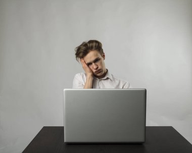 Genç adam internette gezinmek için dizüstü bilgisayar kullanıyor. Yorgun adam. Ağır düşünceler.